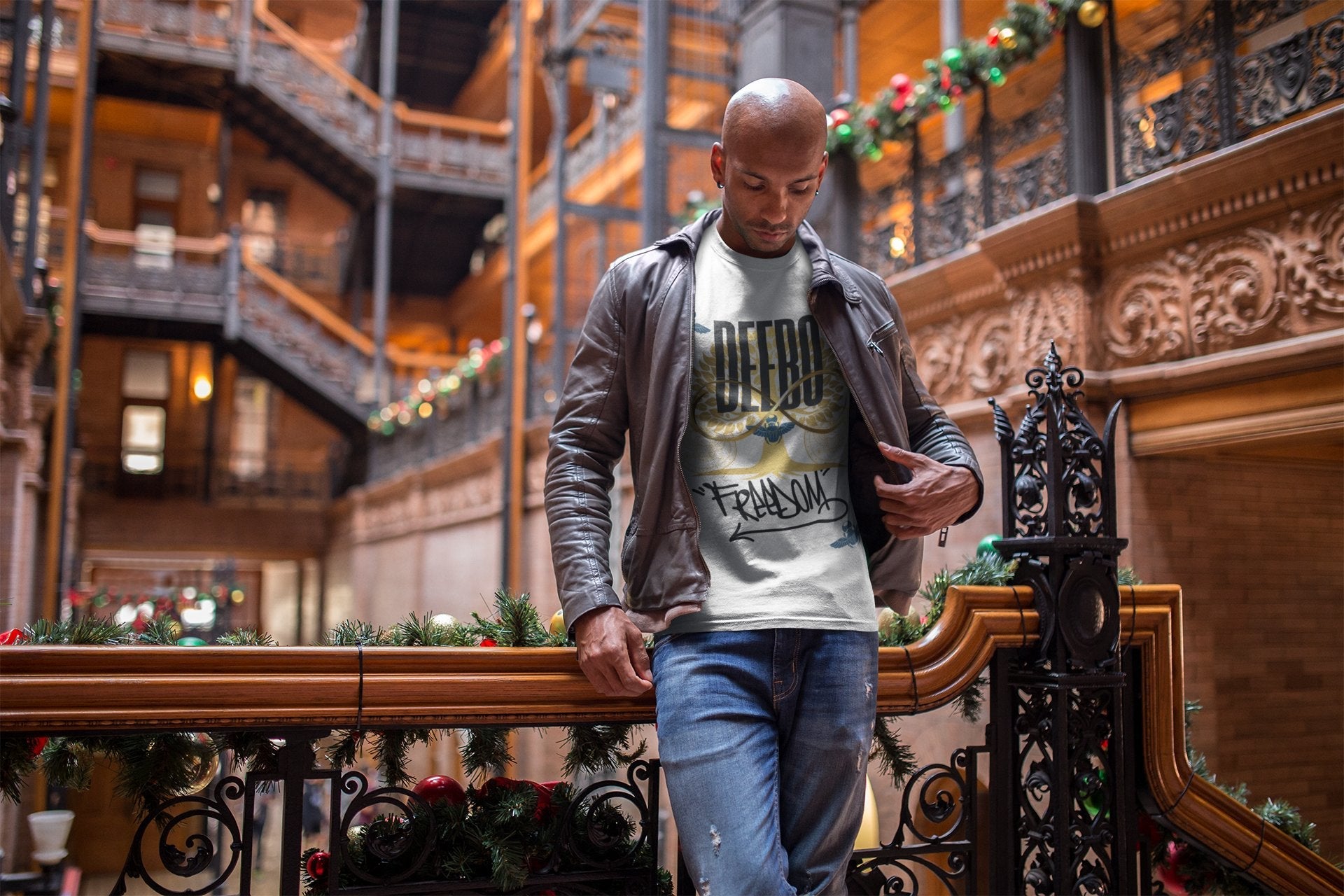 A man in a leather jacket stands on a decorated balcony inside a historic building with ornate ironwork and layered staircases.