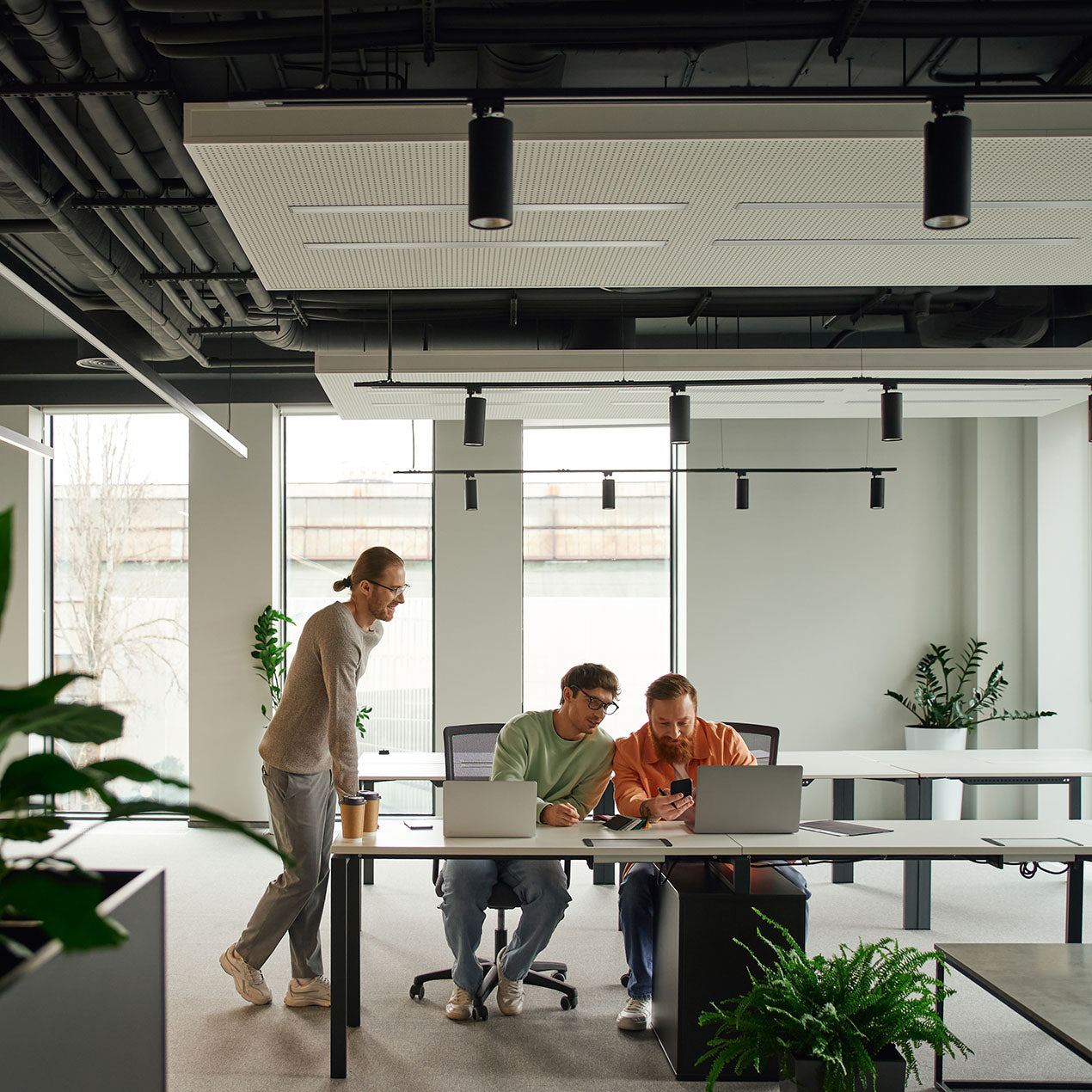 Three men working together in a modern, well-lit office. They are reviewing their SEO performance on a mobile phone.